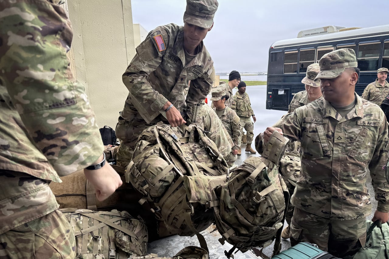 Soldiers in fatigues unloading packs from a vehicle.