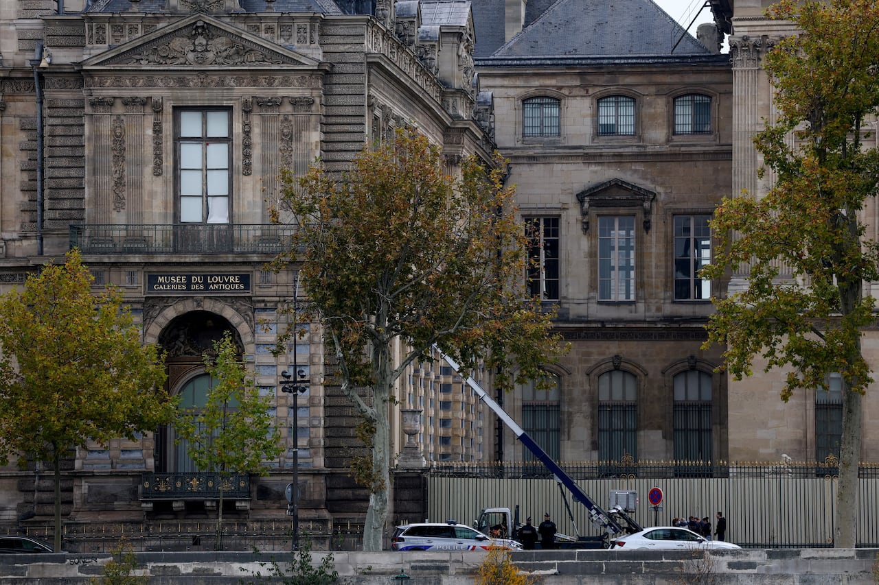 Police officers stand around a small crane leading to a tall window on the second floor of an ornate old building.