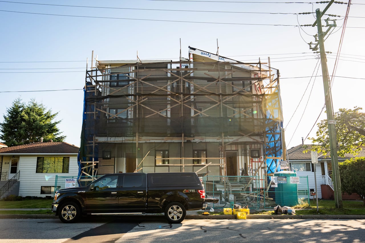 A near complete, still under construction multiplex home that is much taller than the single-family homes on either side