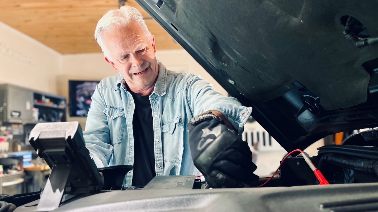 Man in a auto shop working on the front of a car with the hood open