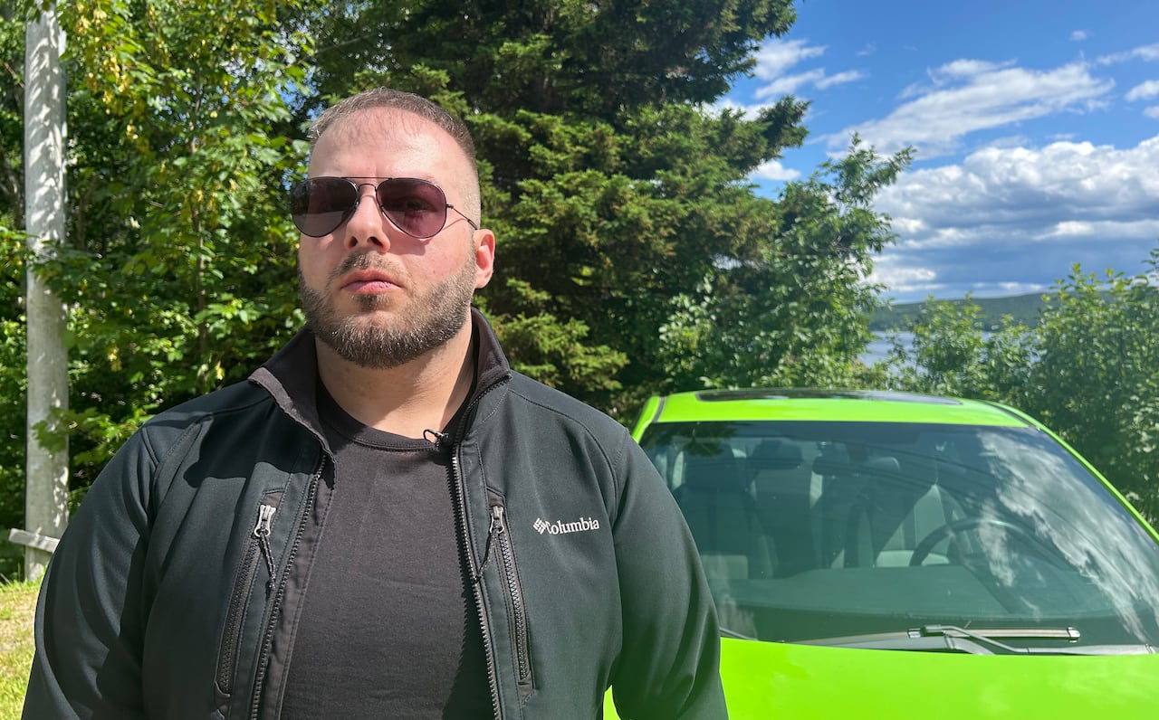 A man wearing sunglasses stands next to a bright green car