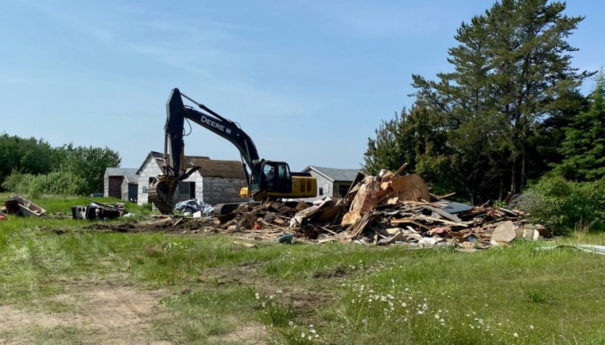 A destroyed home and pieces of wood on a grassy area of land.