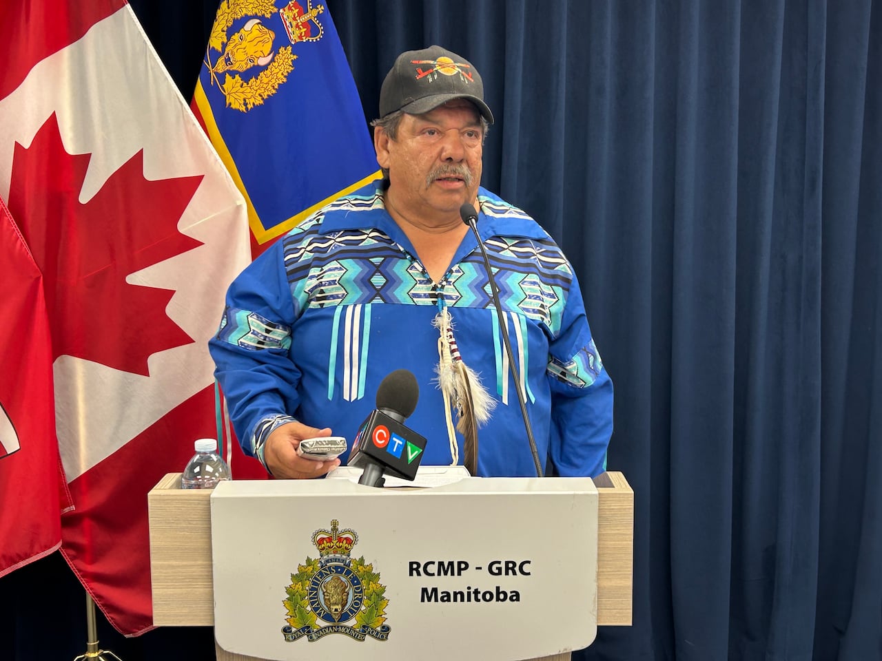 A man wearing a blue t-shirt stands on a podium behind a microphone.