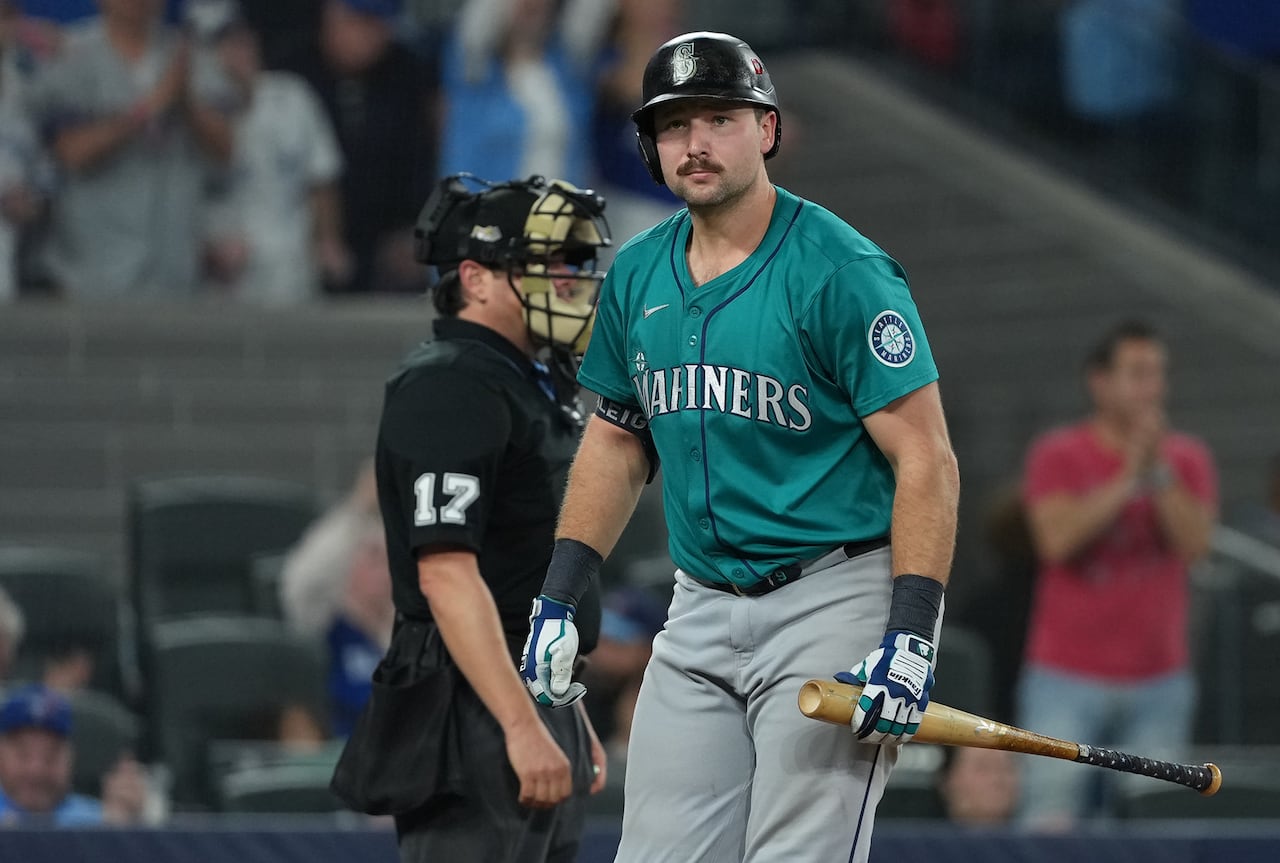A baseball player, holding a bat and wearing a batting helmet, walks away from home plate
