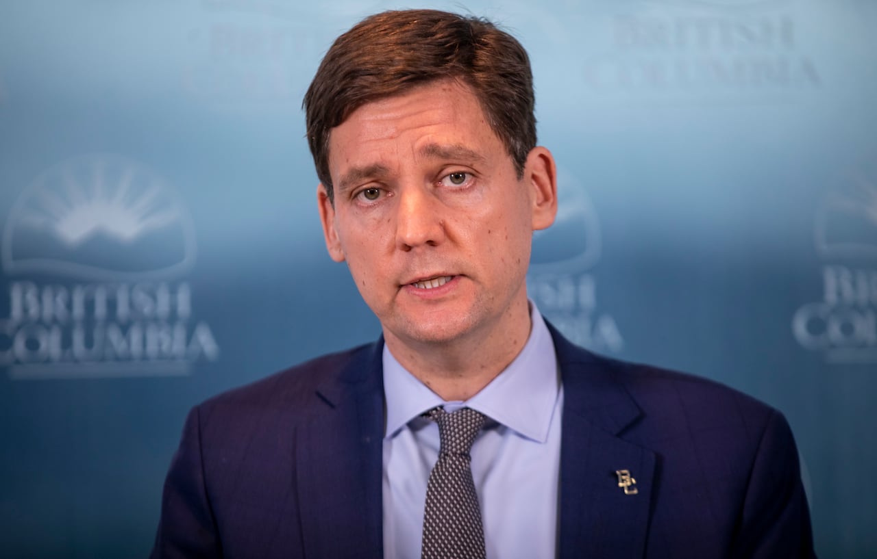 A white man wearing a suit speaks in front of a wall reading 'British Columbia'.
