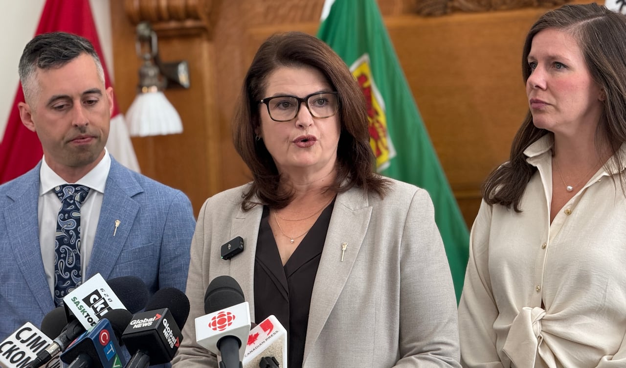 A woman in a grey suit jacket speaks into microphones.