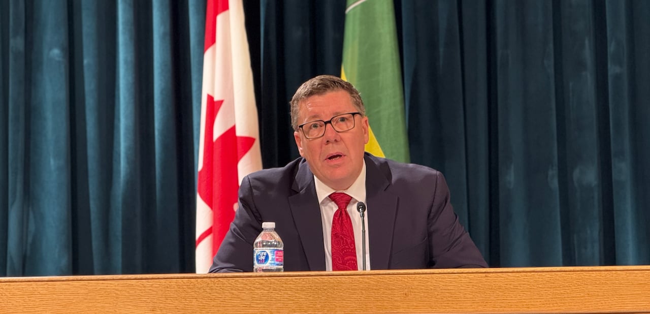 A man in a suit with a red tie sits at a large desk.