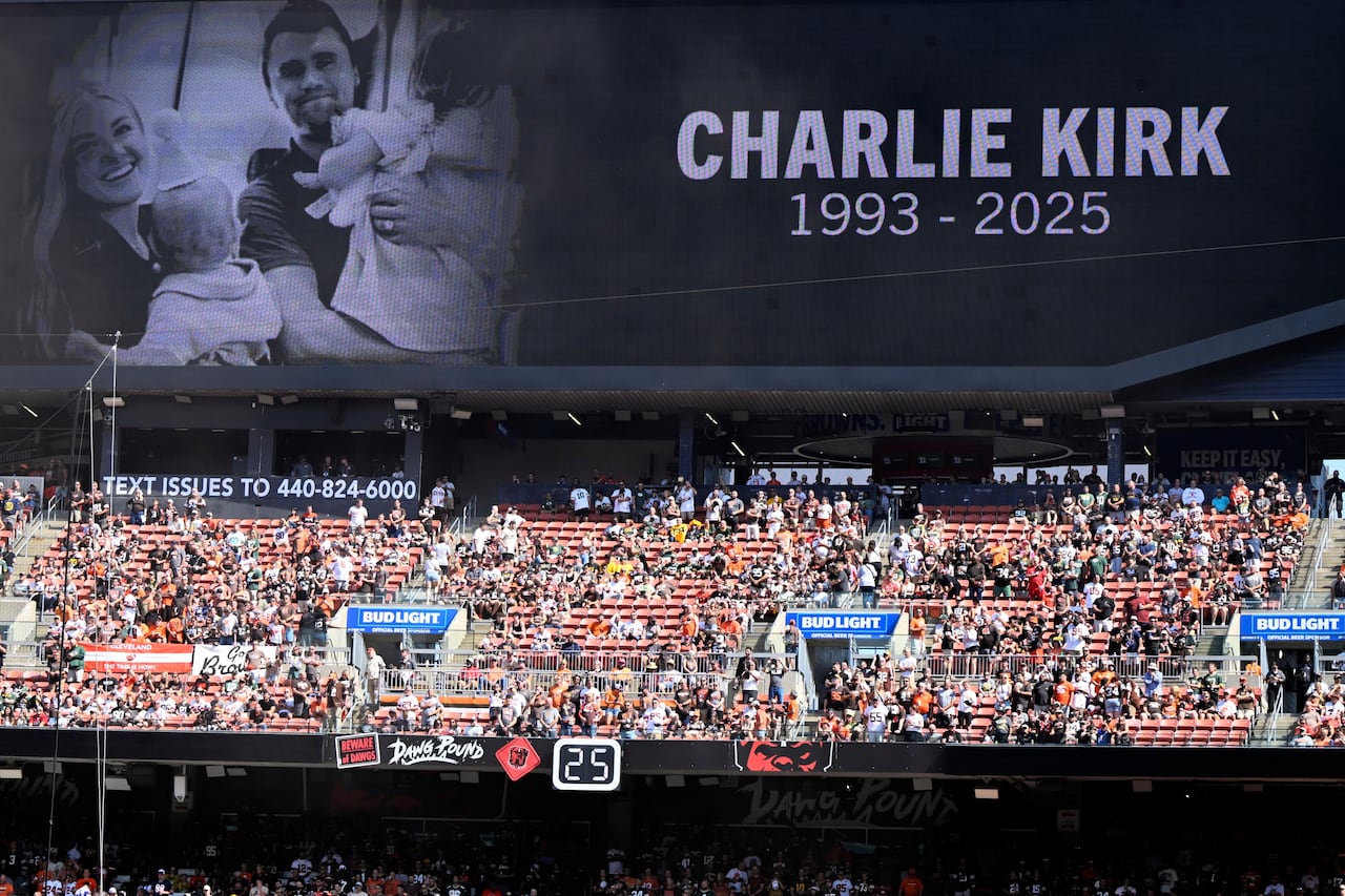 A memorial featuring a photo of a man with his family appears above a large crowd in a stadium.