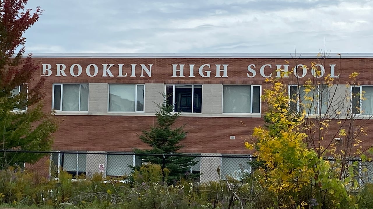 a red brook school stands behind some trees and a fence