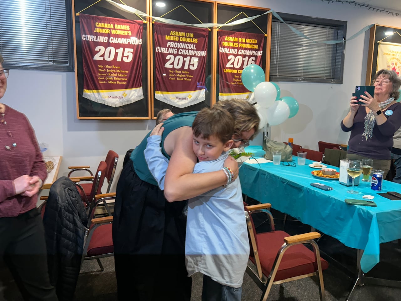 Woman with short hair hugs a young boy in a banquet hall