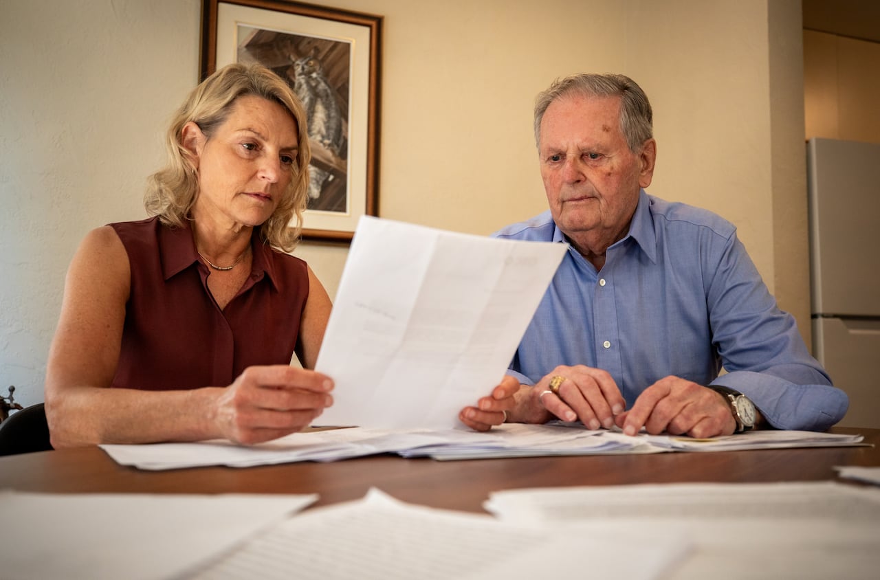 Elderly man and woman sitting at a dining table, looking over documents