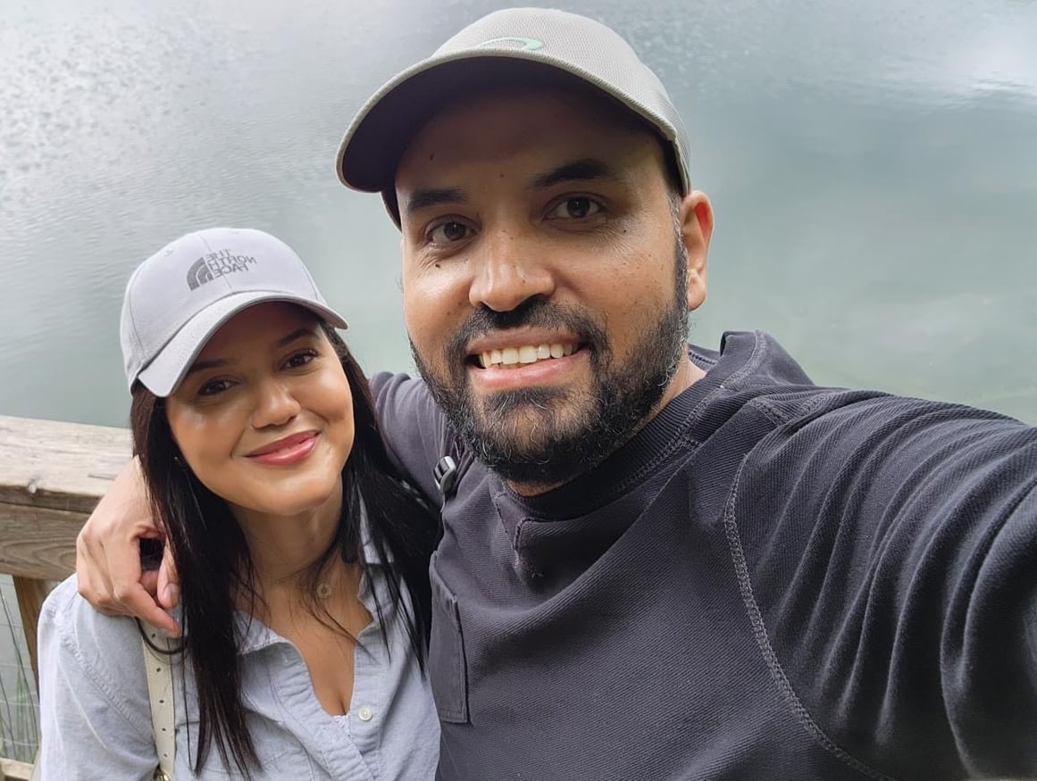 A man and a woman pose for a photo in front of a body of water.