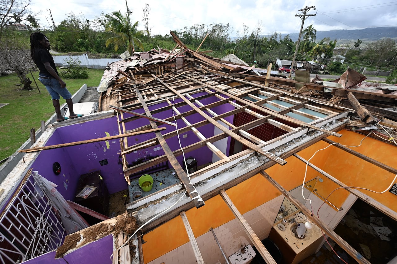 A man stands on what is left of the roof of his neighbor following the passage of Hurricane Melissa, in longwood, St Elizabeth, Jamaica on October 29, 2025.