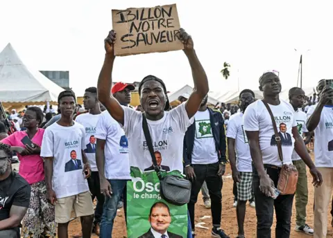 AFP/Getty Images Jean-Louis Billon supporters in white T-shirts supporting him hold up a placard saying in French 'Billon our saviour'.