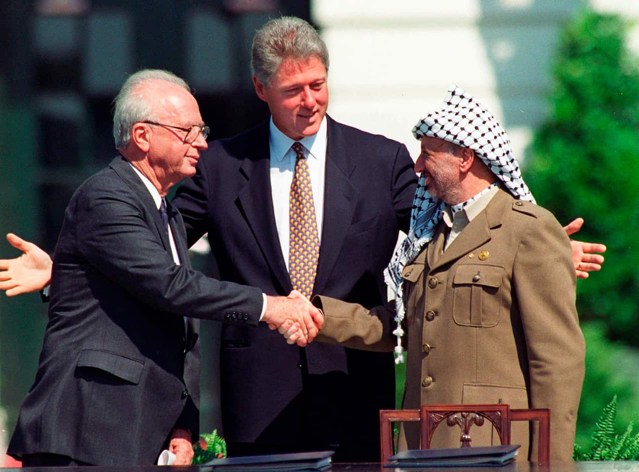 Israeli Prime Minister Yitzhak Rabin (left) and Palestine Liberation Organization Chairman Yasser Arafat (right) shaking hands while US President Bill Clinton (center) watches.