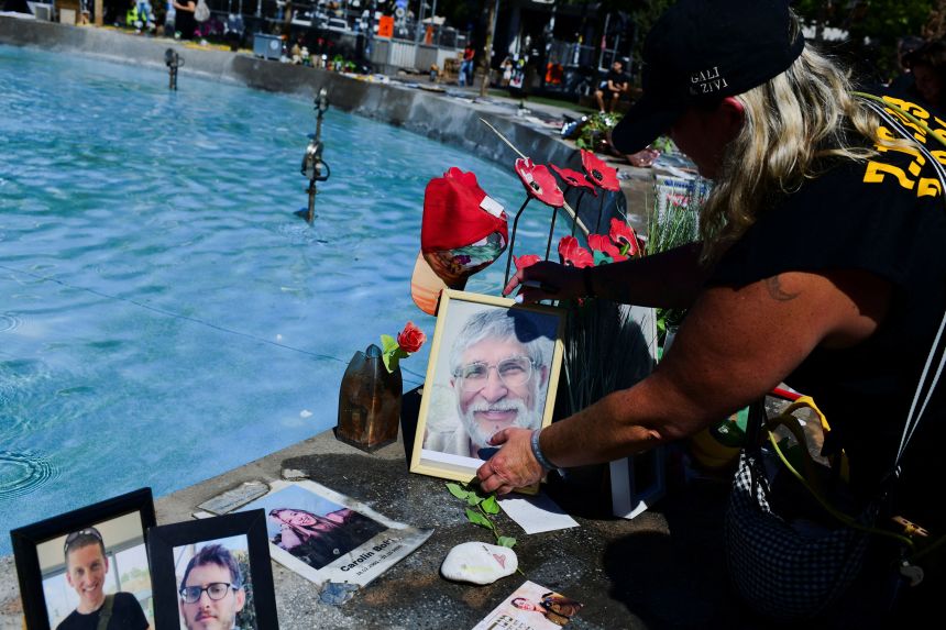 A woman places a picture of slain Israeli hostage Yoram Metzger on Tuesday at a fountain in Tel Aviv which has become an unofficial memorial for hostages, fallen soldiers and victims of the 2023 attack.