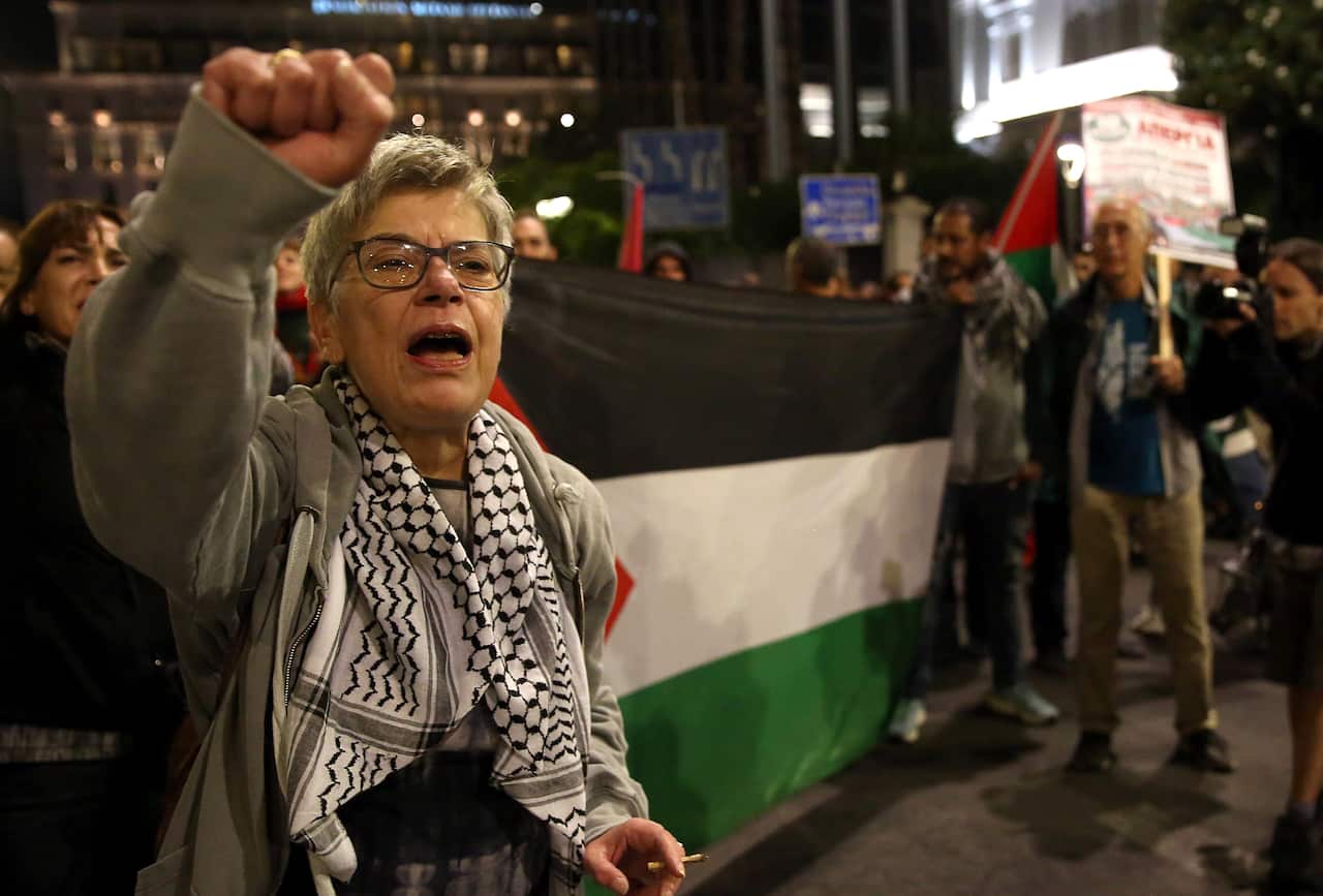 A woman raises her fist against the backdrop of the Palestinian flag during a protest.