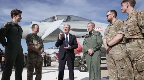 PA Media Sir Keir Starmer speaks with British armed forces personnel as they stand in front of a UK Typhoon fighter jet - they are wearing uniform and he wears a dark suit with navy tie 
