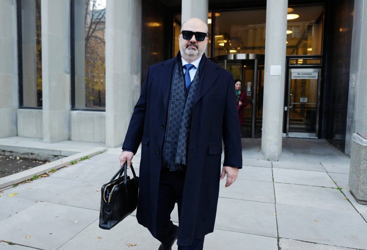 A man in sunglasses, dark suit and an overcoat walking outside a courthouse