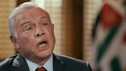 BBC Jordan's King Abdullah, wearing a black suit jacket, pale blue shirt and red tie, speaks with his mouth open