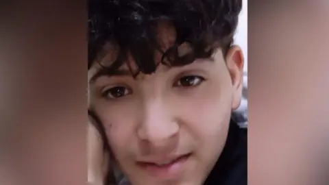 Family handout A teenage boy with a thick black fringe. His face is resting against what appears to be the side of a baby's head.