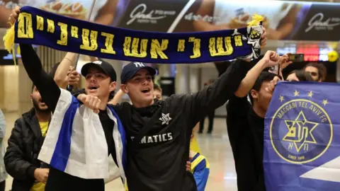 JACK GUEZ/AFP via Getty Maccabi Tel Aviv fans hold up a scarf in the airport before their trip to Amsterdam