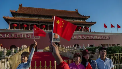 Getty Images Tourists wave the Chinese flag in front of Tiananmen Gate in Tiananmen Square in Beijing China