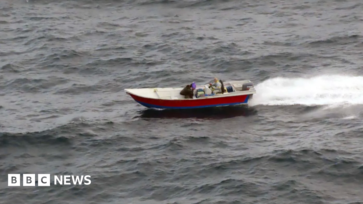 One of the small boats on the water with two people seen in it.