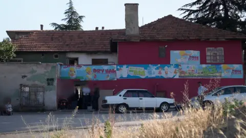 A two-storey building, with the walls painted red, white and green. There are pictures painted on the walls of ducks and children with slogans promoting milk and telling people to eat more fruit and vegetables. 