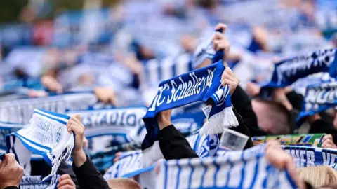 Getty Images A number of fans holding blue and white FC Schalke 04 scarves at a game 