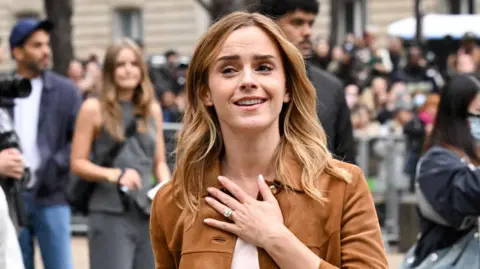 Getty Images Emma Watson poses for the cameras outside the Miu Miu show in Paris, wearing a brown jacket and sporting a ring on her wedding finger.