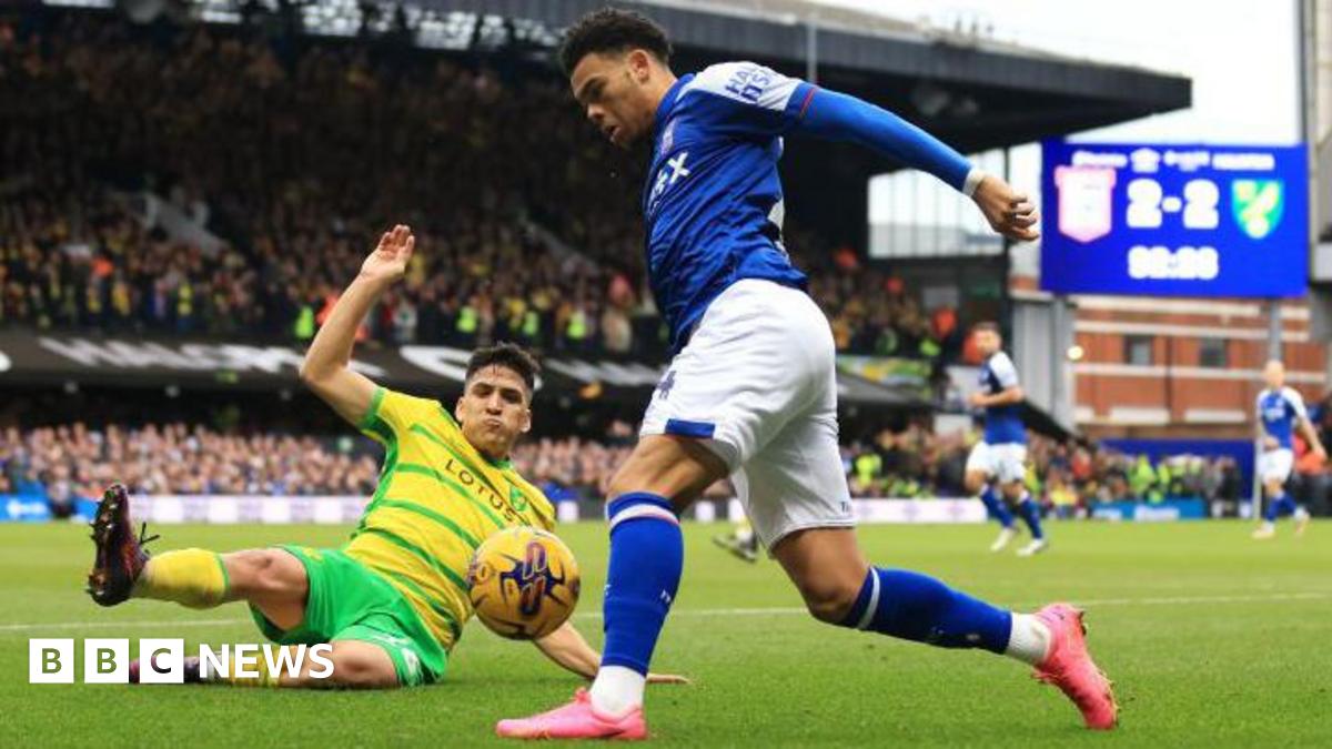 Norwich's Marcelino Nunez is pictured sliding to tackle Dane Scarlett of Ipswich. The scoreboard in the background says 2-2
