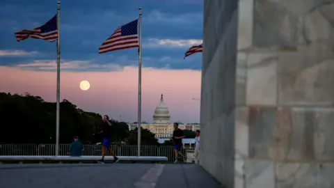 Reuters Supermoon appears in between two US flags, and above US Capitol building in a long shot view of the National Mall.