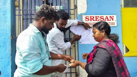Reuters A state health official sticks a notice outside the Sresan Pharmaceutical factory whose Coldrif cough syrup has been linked to the deaths of 17 children in Madhya Pradesh, in Chennai, India, October 7, 2025