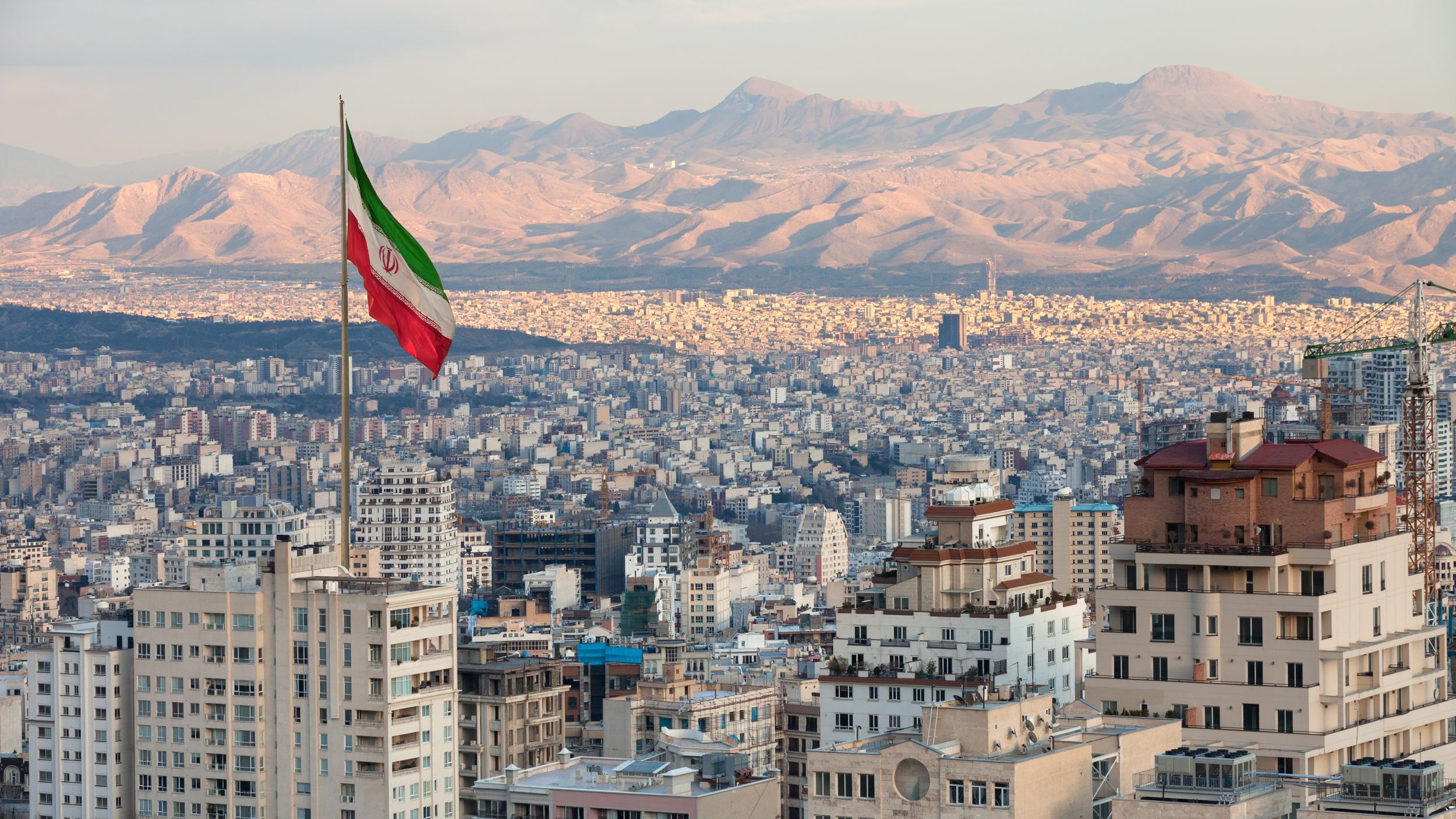 Tehran skyline with an Iran flag in foreground and mountains behind