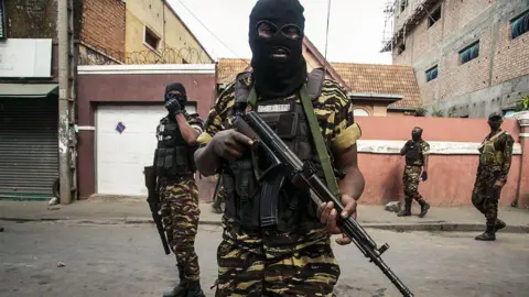 AFP via Getty Images A man in military fatigues and a black ski mask holds an automatic rifle across his chest.