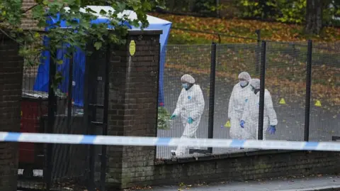 PA Media Three forensic officers wearing white overalls and masks remain at the scene near Heaton Park Hebrew Congregation synagogue. A tent has been erected and a police cordon is in place