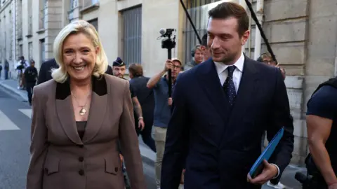 Reuters A smiling Marine Le Pen and Jordan Bardella walk down the street
