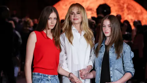 Getty Images Sunday Rose Kidman-Urban, wearing a red vest top and jeans, Nicole Kidman, wearing a white shirt and jeans and Faith Margaret Kidman-Urban in a black top and skirt with a denim jacket.