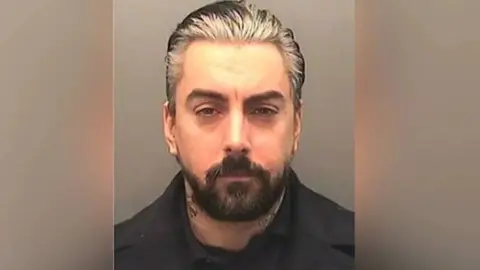 West Yorkshire Police A mugshot of Ian Watkins, a man with slicked back grey hair and a short, dark-haired beard.