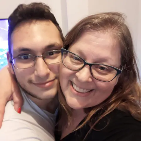 Family handout A woman and a younger man, both wearing glasses, hug and smile at the camera