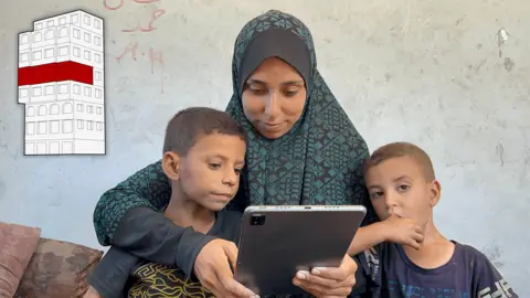 Hadeel and her two young sons look at an iPad. A graphic image of the building is inset in the top left corner of the image, highlighting the fourth floor of the building, where Hadeel lives with her family. 