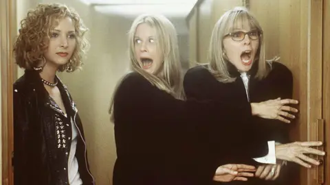 Columbia/Tristar via Getty Images image of Meg Ryan and Diane Keaton holding a door and shrieking as Lisa Kudrow looks on, stone-faced