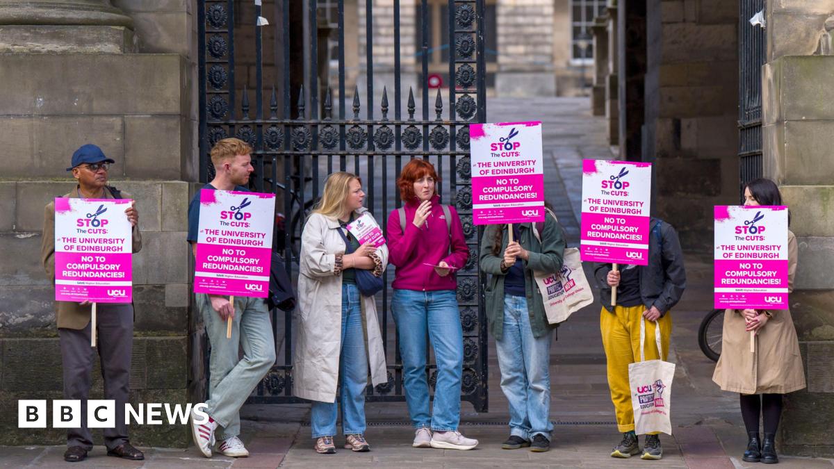 Sanskrity is standing in front of a busy hall. She is wearing a white dress and is looking determinedly at the camera