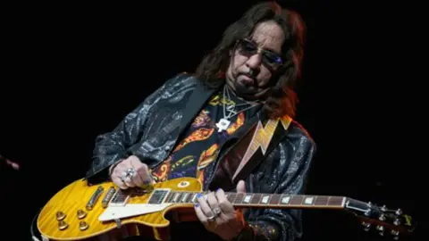 Getty Images Ace Frehley performs, post-KISS, in a glittery black jacket. His guitar strap is emblazoned with a lightning bolt. 