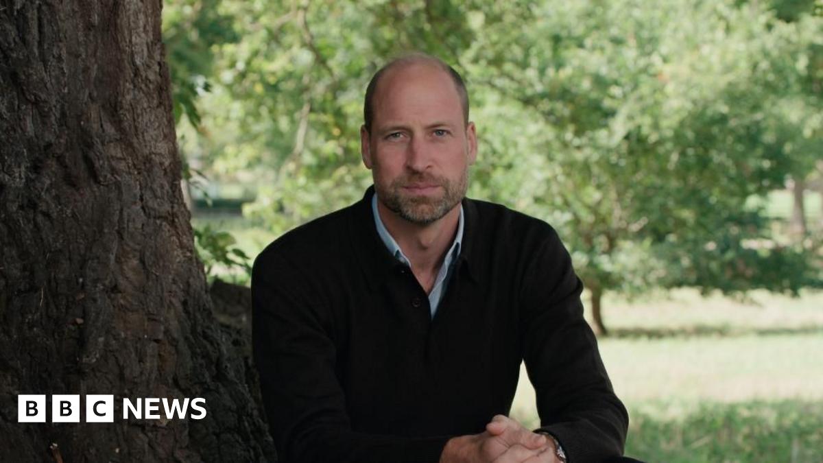 Prince William sits at the foot of a tree looking out beyond the shot of the camera.