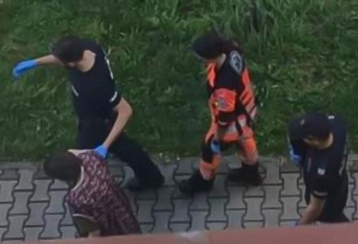 Three emergency responders, two in black uniforms and one in orange gear, escorting a person along a paved path.