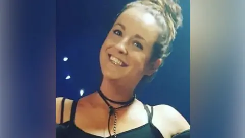 RTÉ Emma Costello McCrory, a woman in a black vest smiles at the camera. She has her hair tied up in a bun