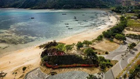 Getty Images Aerial view of a beach lined with green trees. A giant sign that reads "Kuta Mandalika" can be seen on a structure covered by green plants. Boats can be seen floating in the sea in the distance.