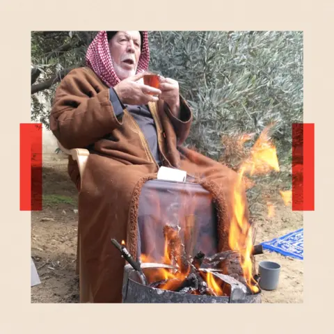 Ayish sitting by a fire
